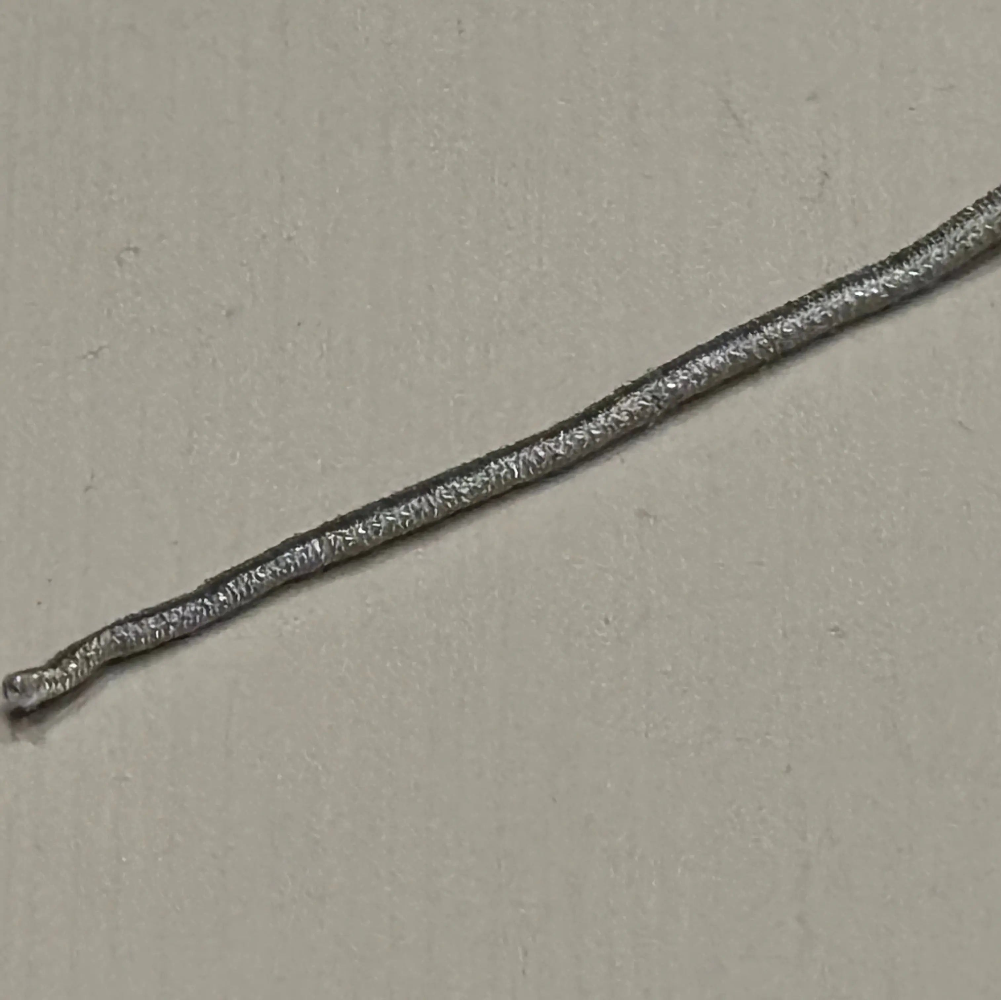 A close-up of a textured silver metallic strip or wire running diagonally across a plain beige background.