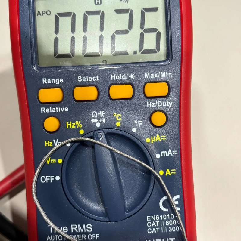 An AstroAI DT132A digital multimeter with a red outer casing, blue rotary dial, and yellow buttons, showing a reading of 00.26 on its LCD screen.